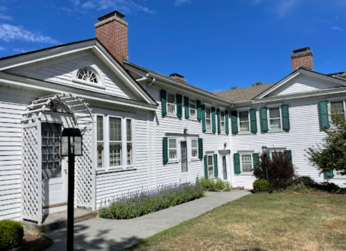 A white, two-story house with green shutters, a stone pathway, and a blue sky in the background.