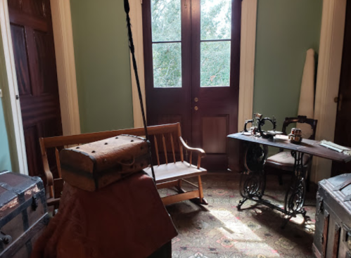 A cozy room with a rocking chair, wooden table, and vintage luggage, illuminated by natural light from the windows.