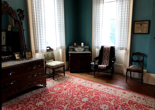 A vintage room with a patterned rug, wooden furniture, and large windows letting in natural light.