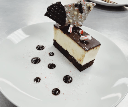 A slice of layered dessert with chocolate, cheesecake, and festive decorations, served on a white plate.