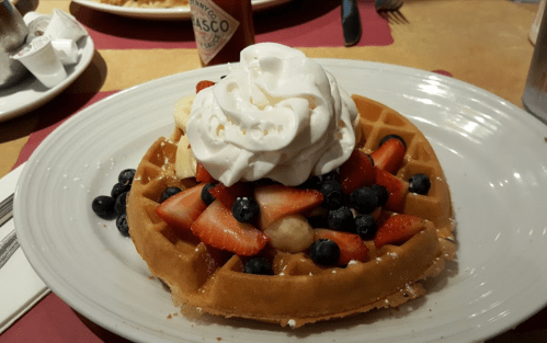 A waffle topped with whipped cream, strawberries, blueberries, and banana slices on a white plate.