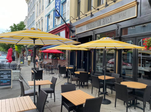 Outdoor seating area of a restaurant with yellow umbrellas, tables, and a welcoming sign.