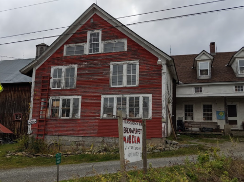 A weathered red barn with white windows and a sign for the Berold-Dupret Museum, set against a cloudy sky.