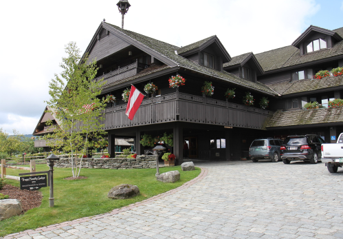 A large wooden lodge with flower boxes, a red flag, and a stone pathway leading to parked cars.