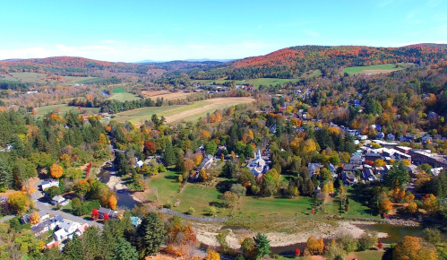 Aerial view of a picturesque rural landscape with colorful autumn foliage, fields, and a small town nestled in the valley.