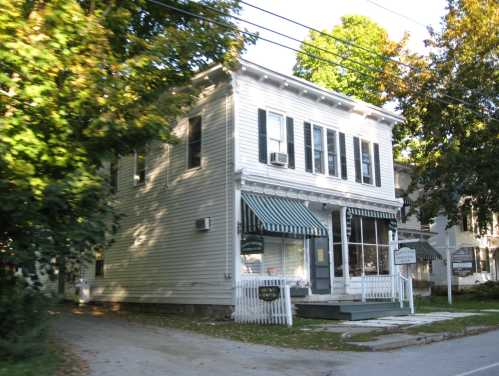 A white two-story building with green awnings, surrounded by trees and a quiet street.