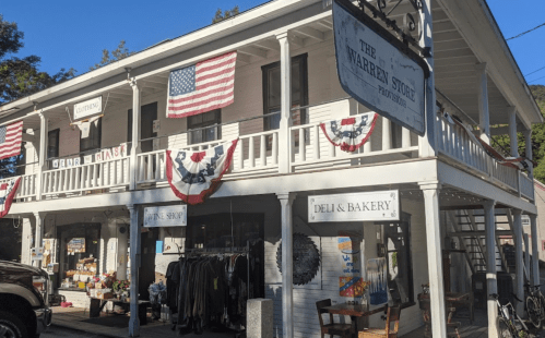 A two-story building with American flags and bunting, featuring shops and a deli/bakery on the ground floor.