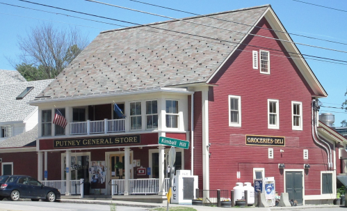 A red two-story building with a sign for Putney General Store and Grocer's Deli, located at a street intersection.