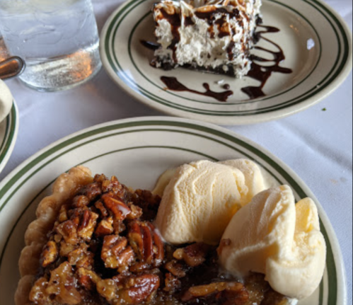A slice of pecan pie with two scoops of ice cream, alongside a plate of chocolate dessert topped with whipped cream.