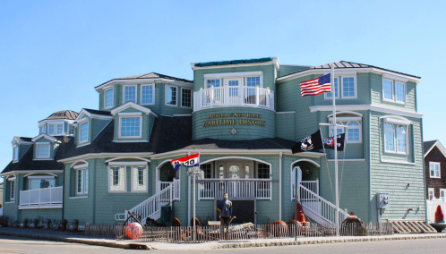 A large, light blue building with multiple gables, flags, and a porch, resembling a seaside museum.