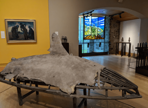A whale skeleton displayed in a museum, with a stained glass window and artwork visible in the background.
