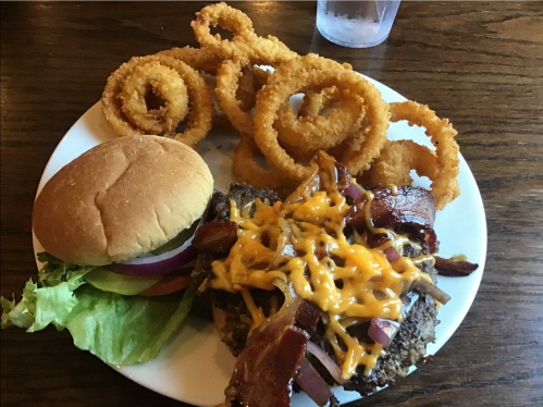 A plate with a burger topped with bacon and cheese, served with a side of crispy onion rings.