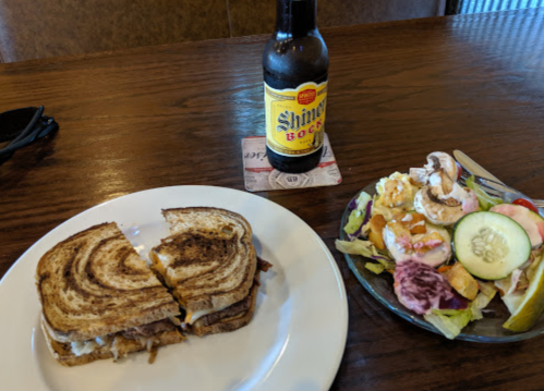 A plate with a grilled sandwich, a side salad, and a bottle of Shiner beer on a wooden table.