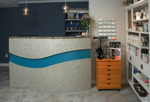 Modern reception area with a curved desk featuring a blue accent, surrounded by shelves of products and an orange storage unit.