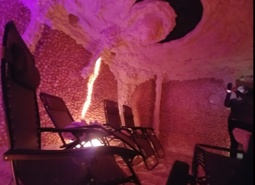A serene salt therapy room with pink lighting, featuring reclining chairs and textured salt walls.
