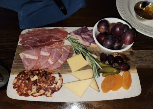 A charcuterie board featuring meats, cheeses, olives, grapes, pickles, and dried fruit on a wooden platter.