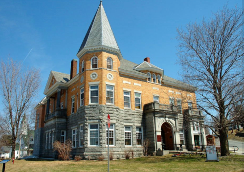 Historic building with a stone and brick facade, featuring a pointed roof and large windows, set against a clear blue sky.