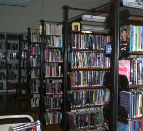 A library interior with tall bookshelves filled with books, a chair visible, and a quiet, organized atmosphere.