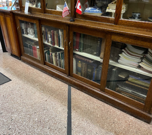 A wooden display cabinet with glass doors, showcasing books and decorative items, with flags of the USA and Canada.