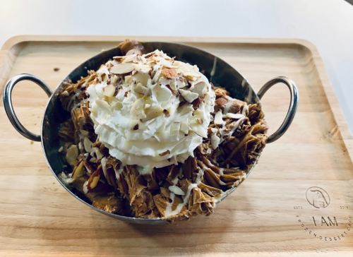 A bowl of dessert topped with whipped cream and sliced almonds, served on a wooden tray.
