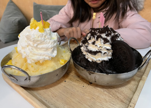 Two bowls of dessert: one with shaved ice topped with whipped cream and mango, the other with chocolate and Oreo cookies.