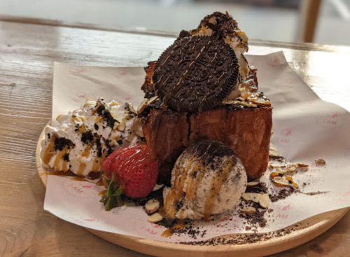 A dessert plate featuring a thick slice of bread topped with whipped cream, an Oreo cookie, a strawberry, and ice cream.