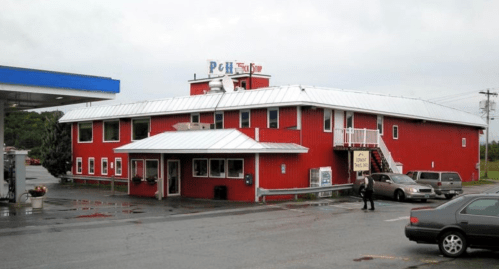 A red two-story building with a metal roof, featuring a gas station and parking area in front.