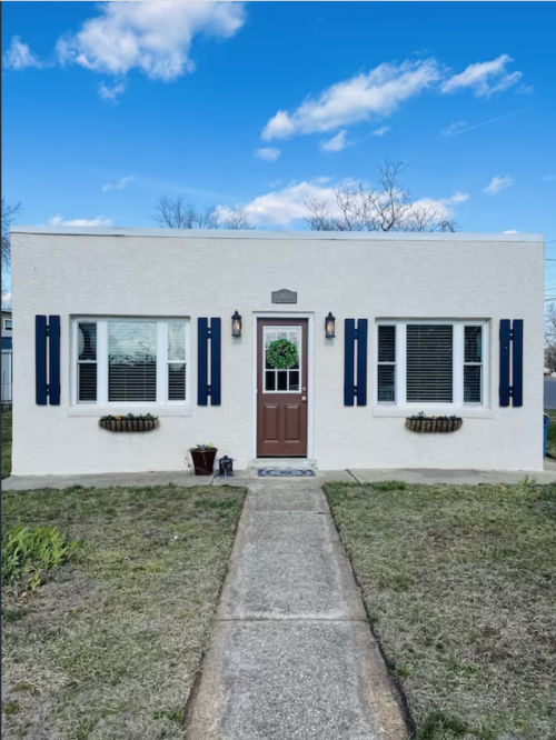 A charming white house with blue shutters, a brown door, and a small garden path leading to the entrance.