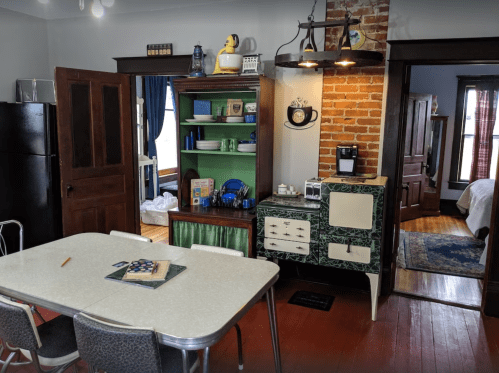 A cozy kitchen with a dining table, vintage appliances, and exposed brick walls, leading to a bedroom.