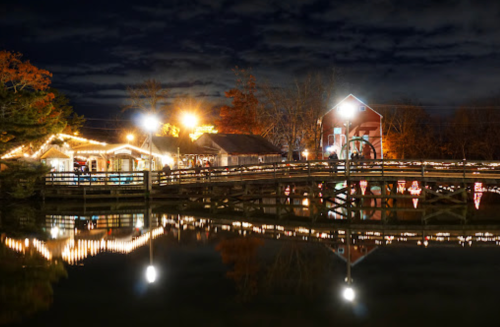 A serene night scene of a bridge and buildings adorned with lights, reflecting in calm water under a starry sky.