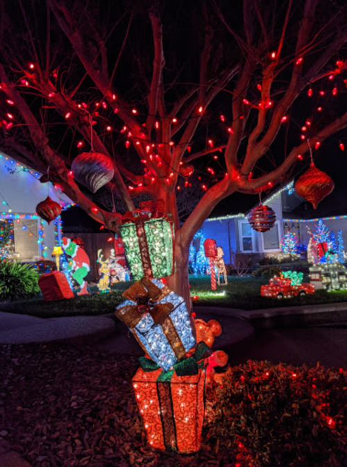 Colorful holiday decorations with illuminated gifts and ornaments on a tree, set against a festive backdrop.