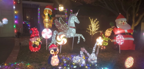Colorful holiday decorations featuring a unicorn, Santa, penguin, and various lights in a festive yard display.