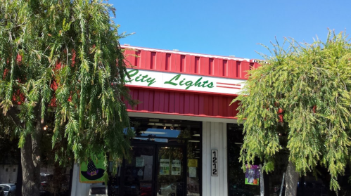 Storefront of "City Lights" with green signage, red awning, and trees in front under a clear blue sky.