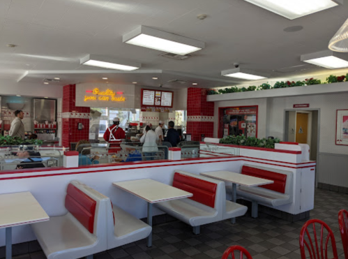 Interior of a fast-food restaurant with red and white decor, featuring booths and a counter with customers ordering.