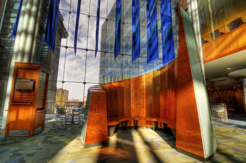 Modern interior space with wooden seating, large windows, and colorful banners, illuminated by natural light.