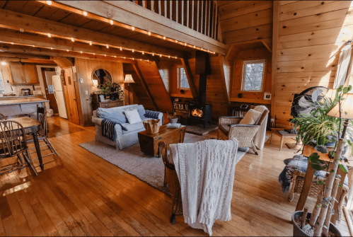 Cozy wooden cabin interior with a living area, dining space, and warm lighting, featuring a fireplace and comfortable furniture.