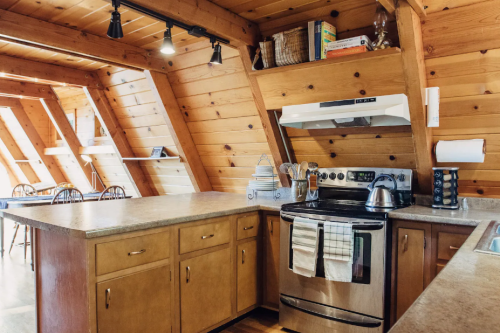 Cozy kitchen with wooden walls, modern appliances, and a spacious countertop, featuring a dining area in the background.