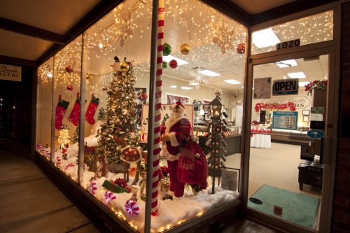 A festive storefront decorated with a Christmas tree, stockings, lights, and a Santa figure in a snowy scene.