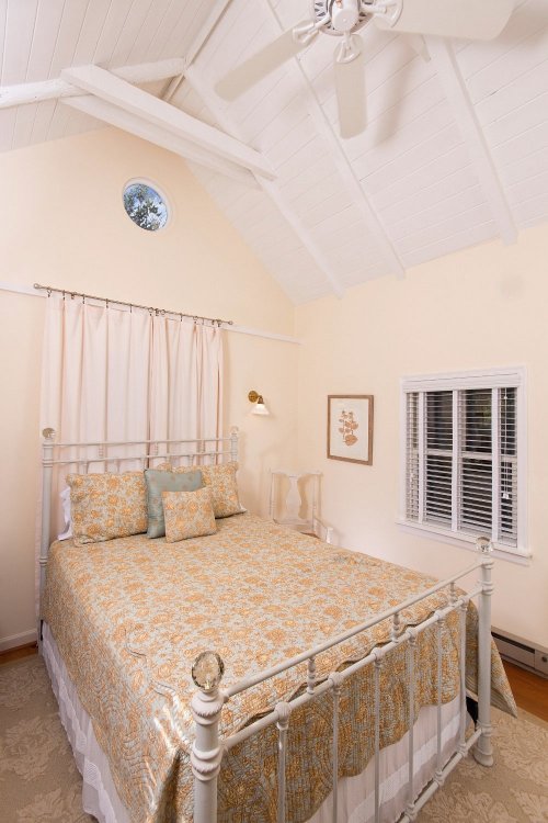 Cozy bedroom with a white metal bed, floral bedding, and natural light from a window and round ceiling vent.