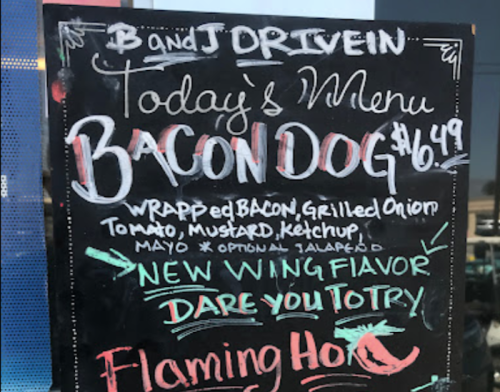 A chalkboard menu featuring a Bacon Dog for $6.49, with toppings like grilled onion, tomato, mustard, and optional jalapeño.