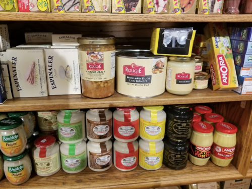 A wooden shelf filled with various jars of duck fat products and canned goods, showcasing gourmet food items.
