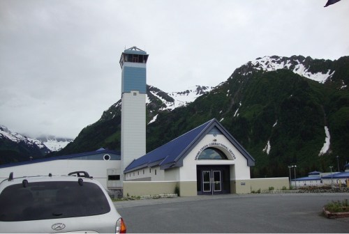 A correctional facility building with a tall watchtower, surrounded by mountains and cloudy skies.