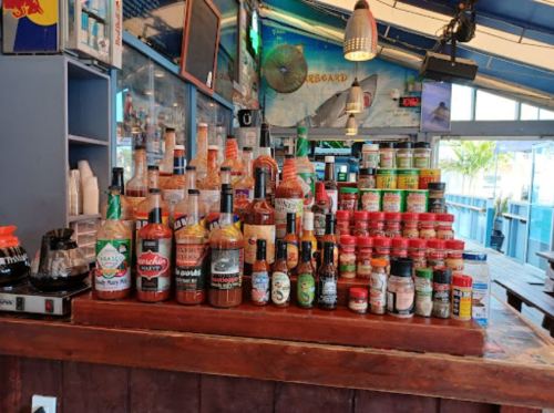 A bar counter displaying various bottles of sauces, spices, and drinks in a vibrant, casual setting.