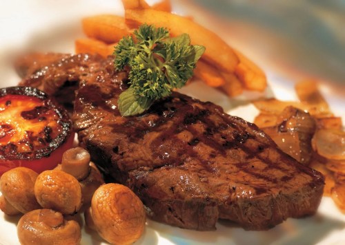 A grilled steak served with fries, a grilled tomato, mushrooms, and a garnish of parsley.