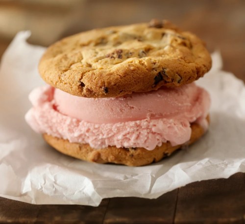 A delicious ice cream sandwich made with two chocolate chip cookies and a scoop of pink ice cream in the middle.