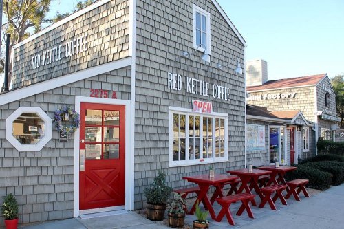 A cozy coffee shop with a red door and outdoor seating, featuring a shingled exterior and an "Open" sign.