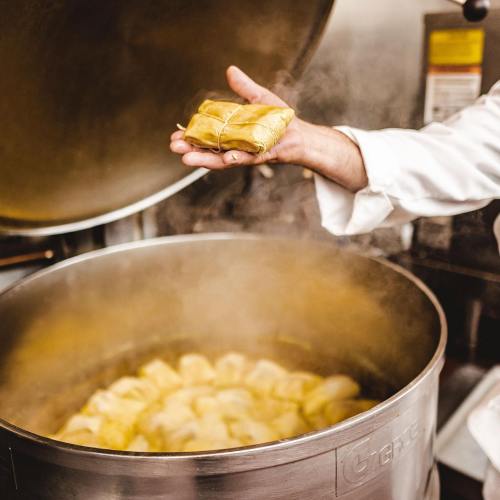 A chef holds a wrapped dish above a steaming pot filled with similar items.
