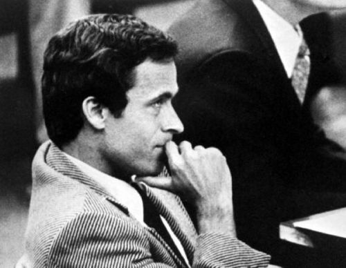 A man in a striped suit sits thoughtfully, resting his chin on his hand in a courtroom setting.