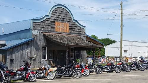 A rustic building with a sign reading "The Knobbed Bone" and a row of parked motorcycles in front.
