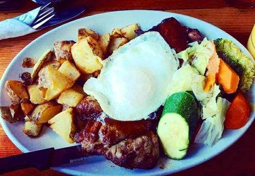 A hearty plate of food featuring steak, a fried egg, potatoes, and mixed vegetables.